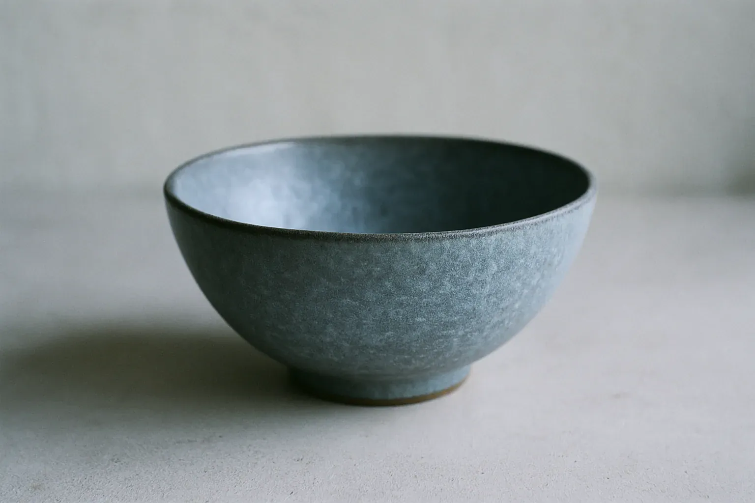 A satin matte ceramic bowl with a mottled crystalline surface on a studio table, warm kiln glow behind